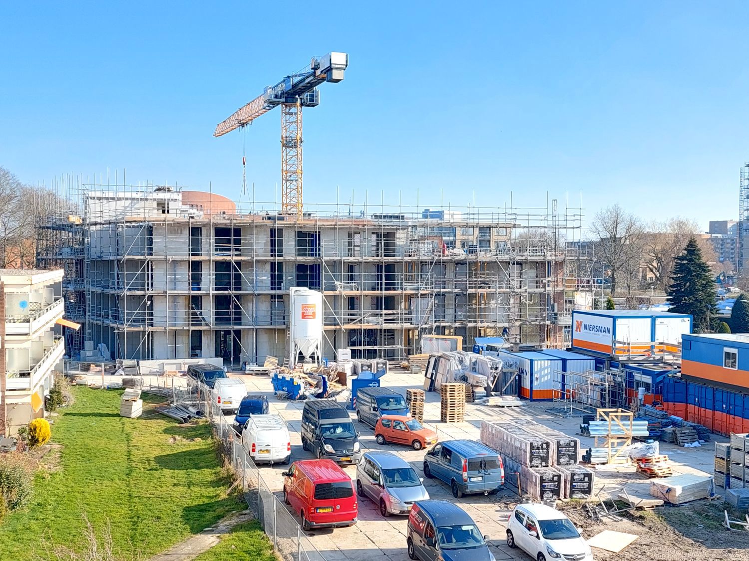 Foto met zicht op bouwterrein en in achtergrond gebouw in aanbouw in steigers vier hoog