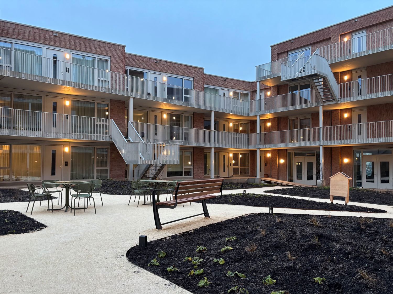 Avondfoto met lampjes bij de woningen drie hoog appartementen en binnentuin met bankje