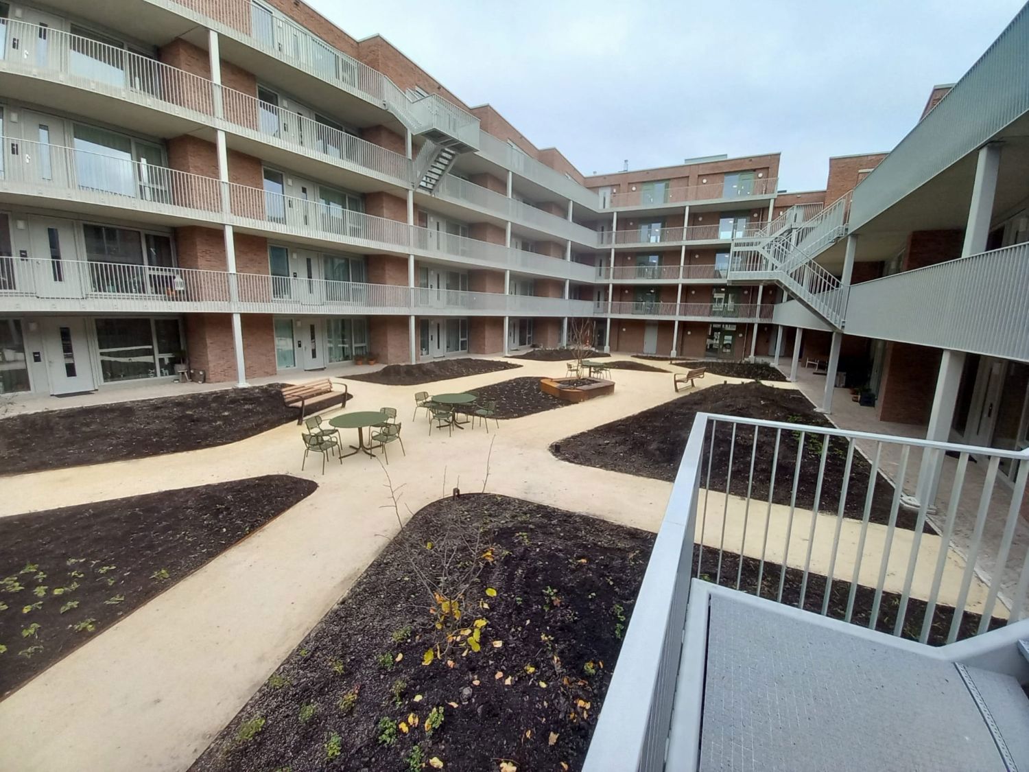 Foto van de binnentuin met gele zandpaden en aarden perken met bankje